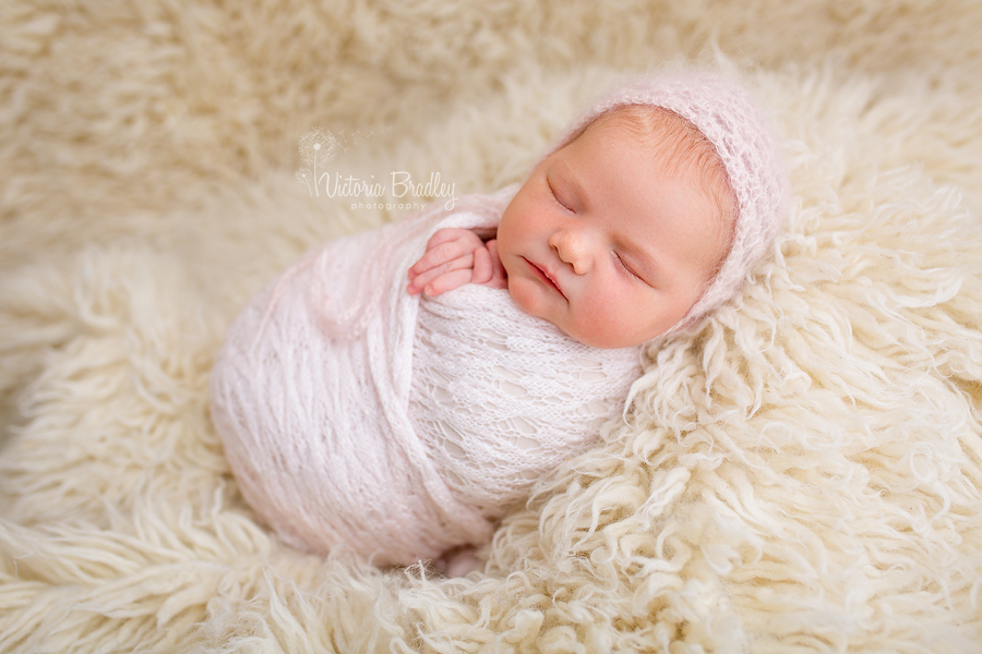 wrapped baby during a newborn photography session, in a pink knitted wrap with pink bonnet